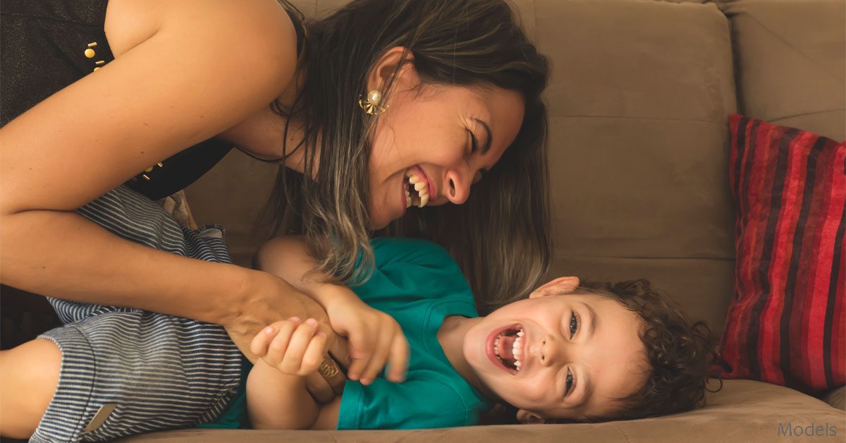 Mother Tickling Laughing Son on Couch