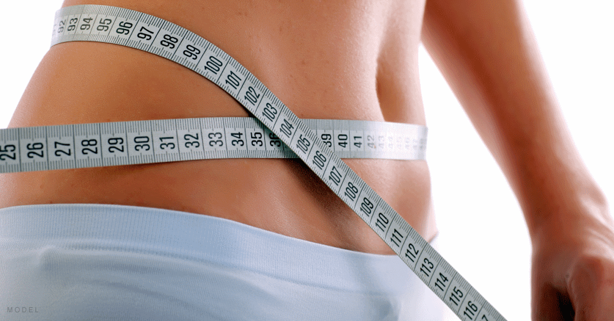 A woman measures her waist while contemplating a tummy tuck.