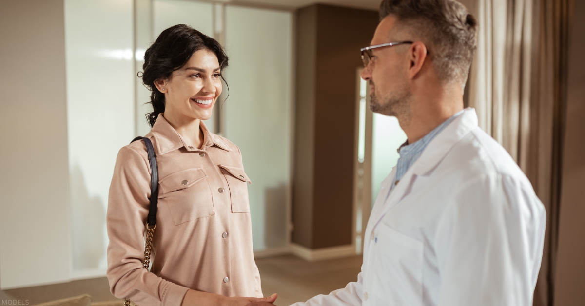 Plastic surgeon and patient shaking hands in a medical office setting. (models)