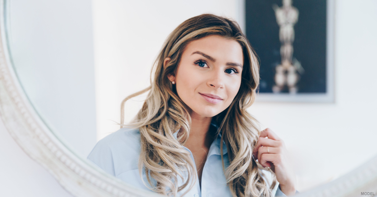 A woman in Denver, CO is looking in a mirror to see her healthy, glowing skin.