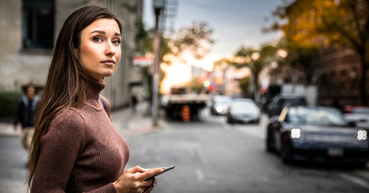 A woman who has recovered from breast augmentation surgery walks along a Denver street with her mobile phone.