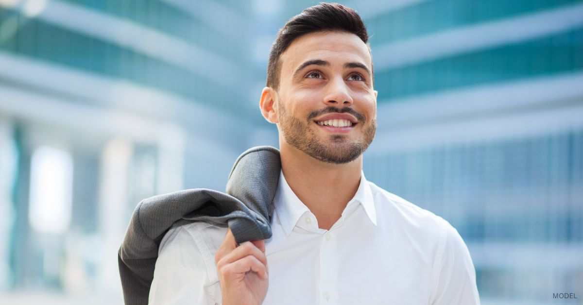 Confident businessman (model) holding a suit jacket over his shoulder.